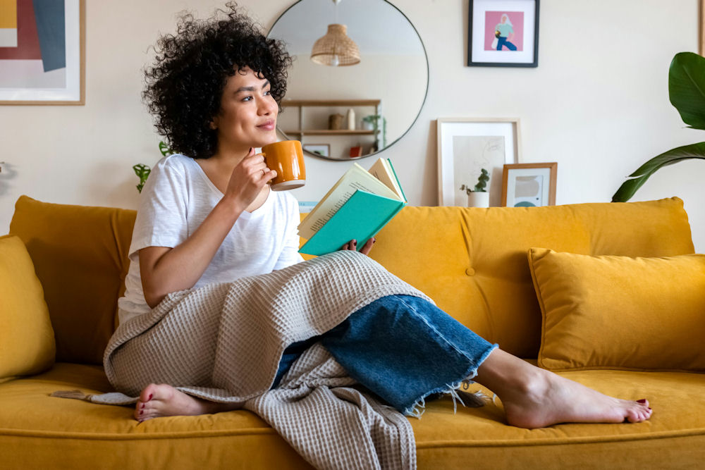 woman-sitting-on-couch-drinking-tea-and-reading-a-book