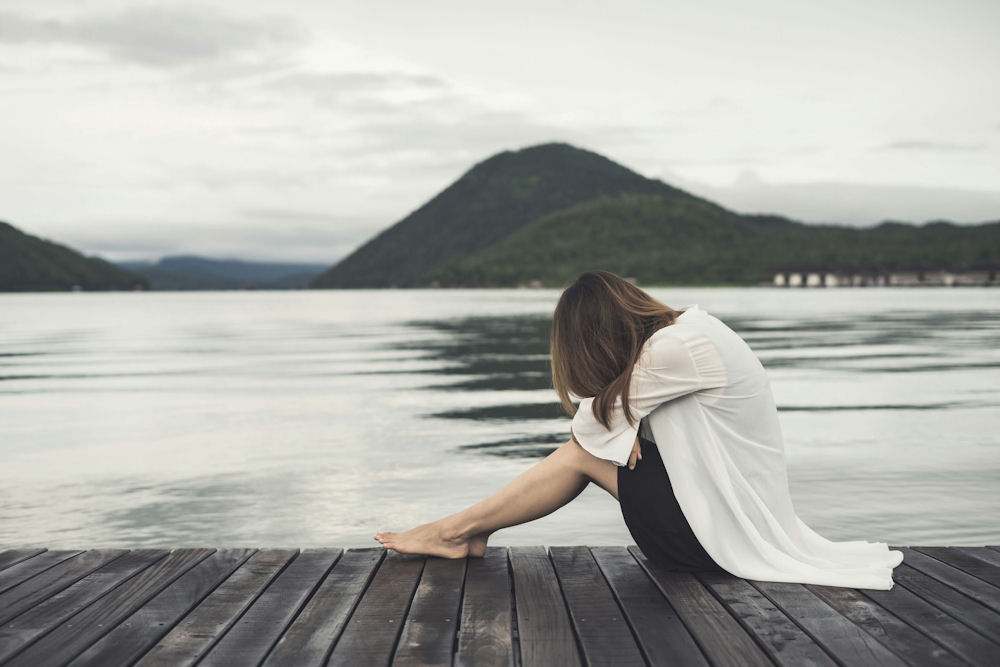 a-woman-with-her-head-down-sitting-on-a-pier