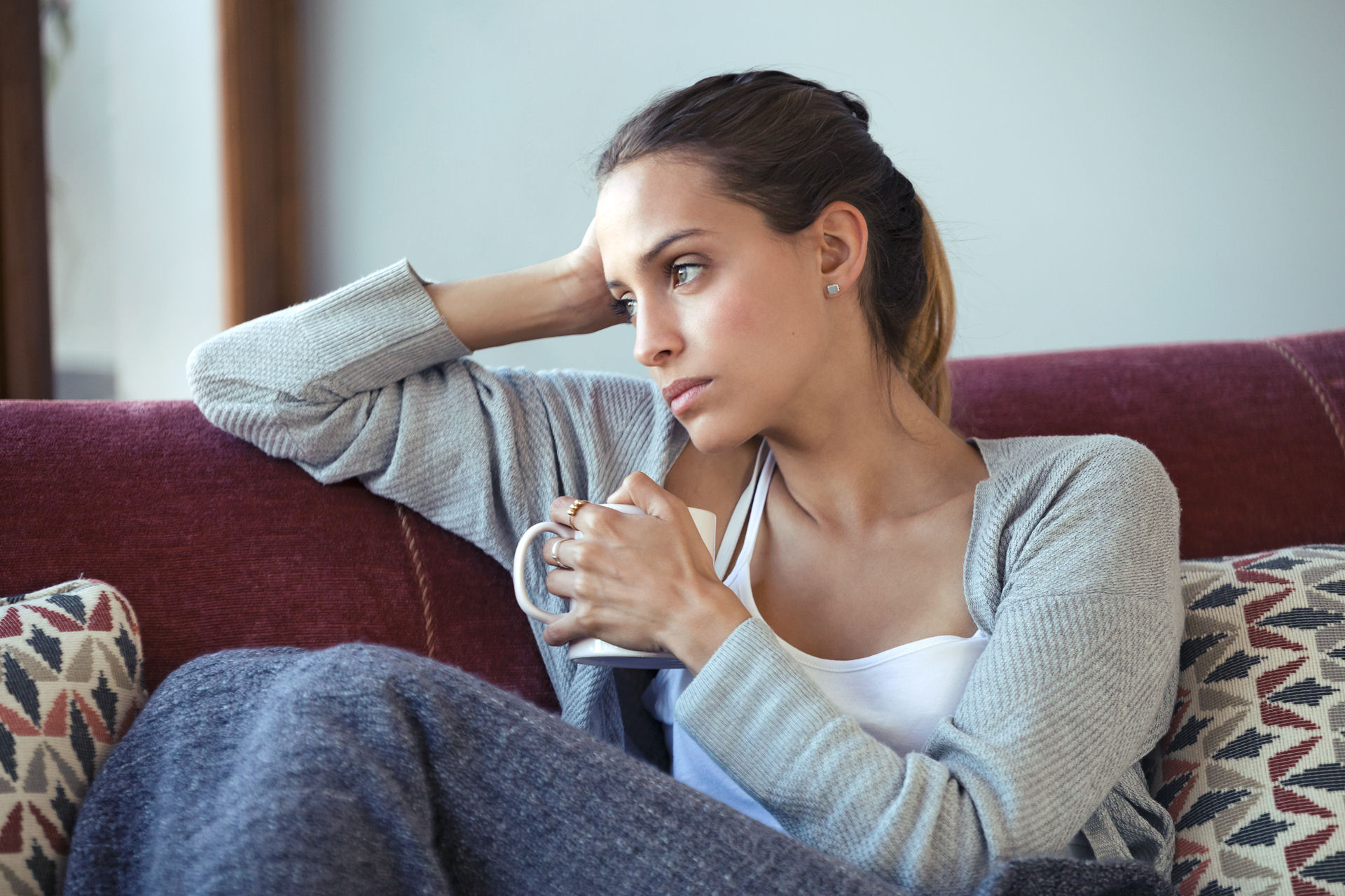woman staring off into the distance with a sad expression while sitting down with a cup of coffee