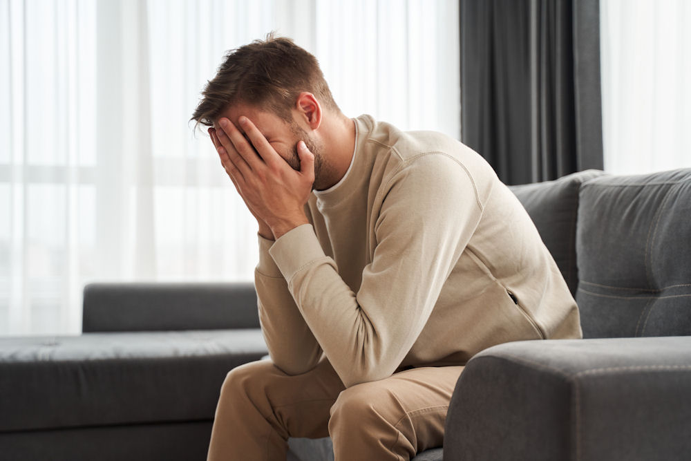 upset man with face in his hands sitting on a chair