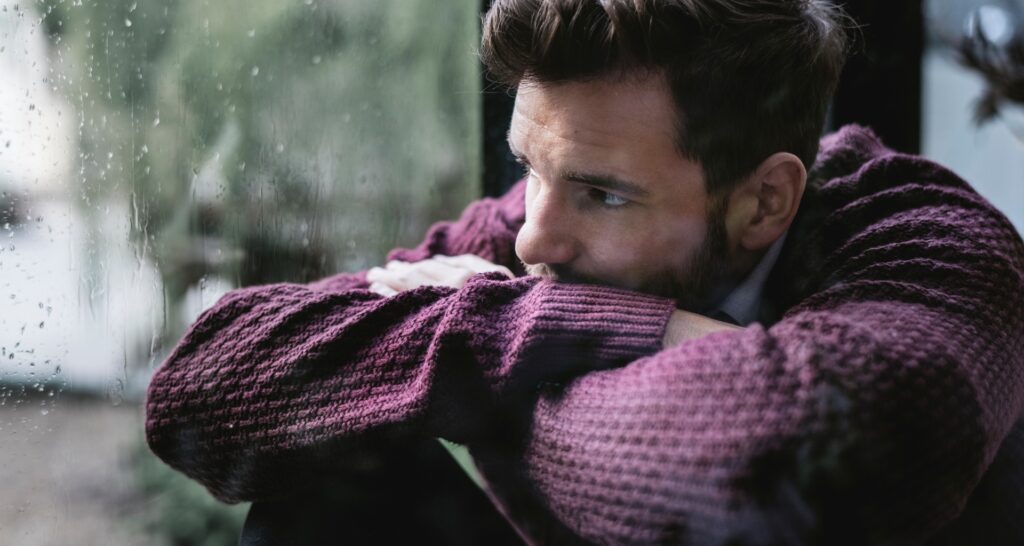 a somber man looking out a window