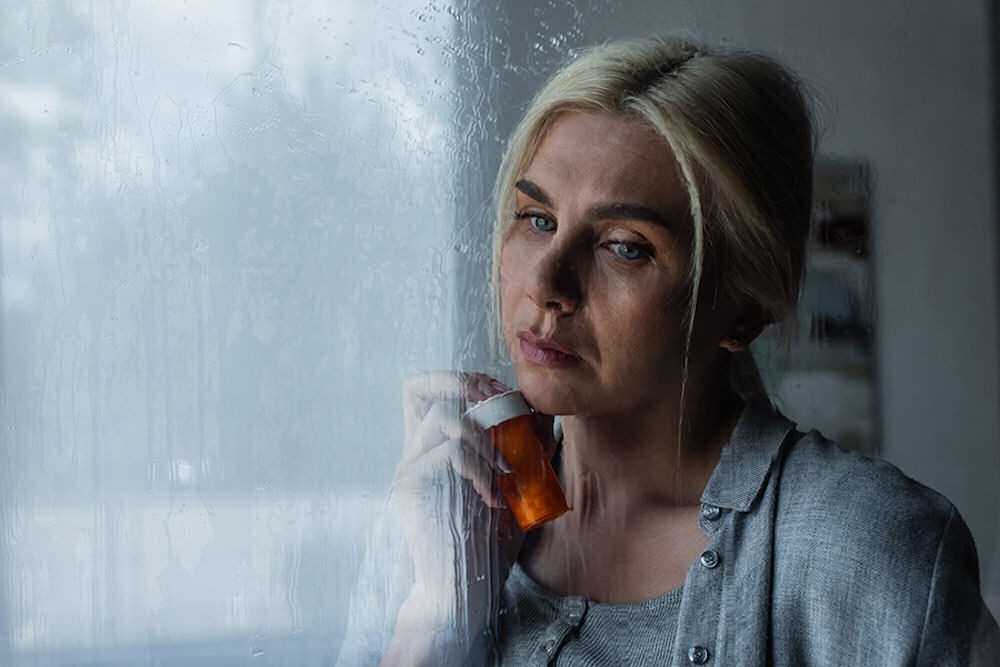woman standing by a window holding her medication