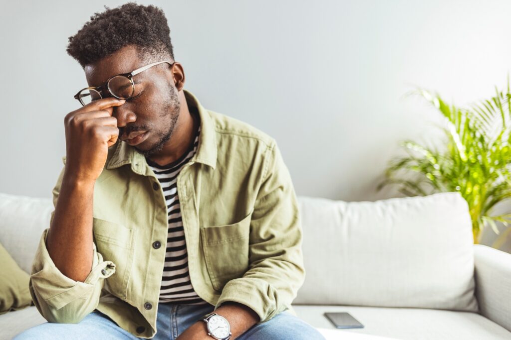 man sitting on couch during therapy session rubbing his eyes