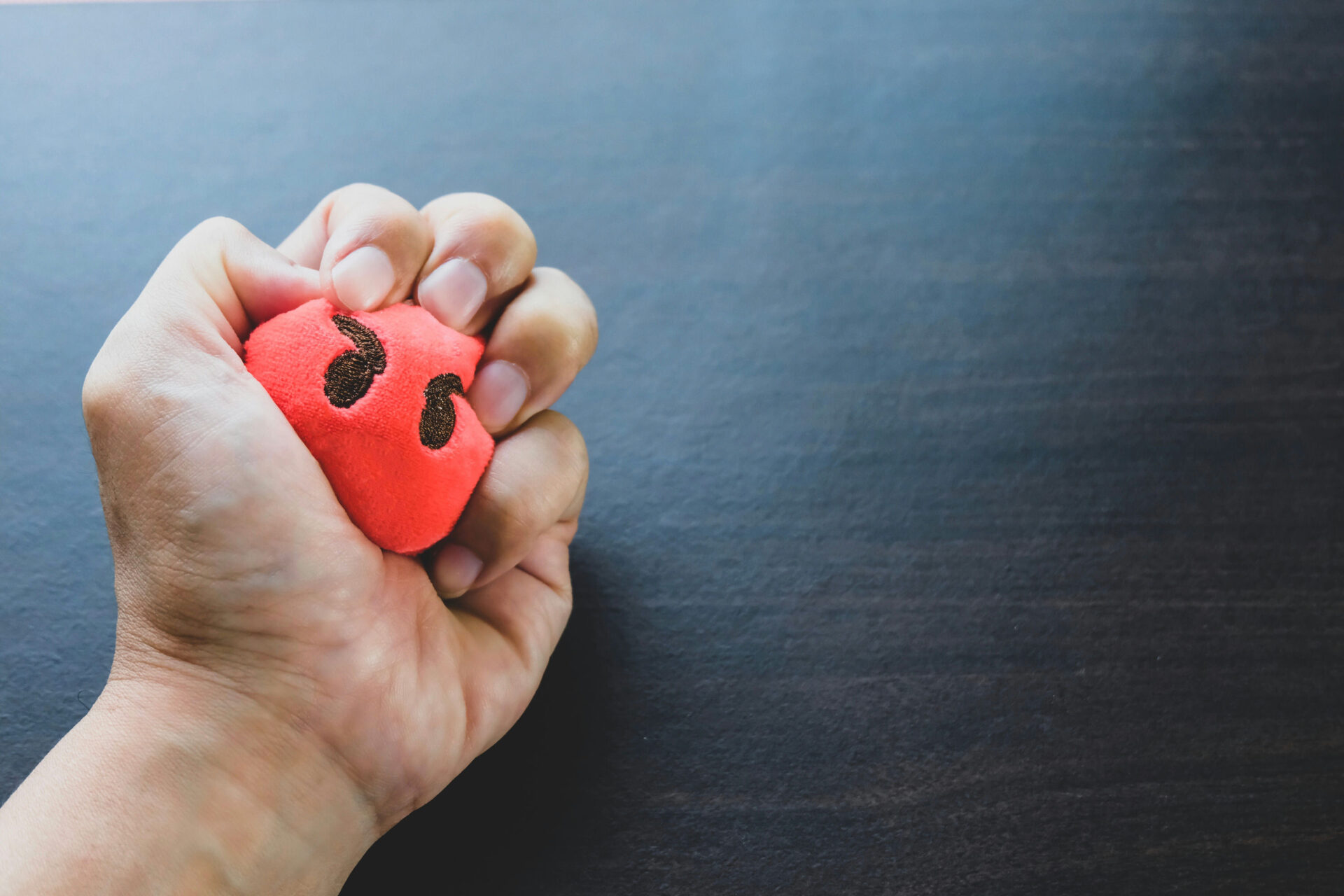 person squeezing a stress ball with an angry face on it
