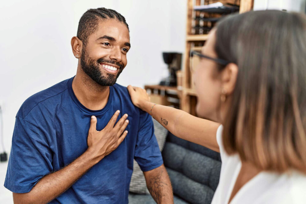 man wearing a blue shirt smiling and touching his chest while meeting his therapist